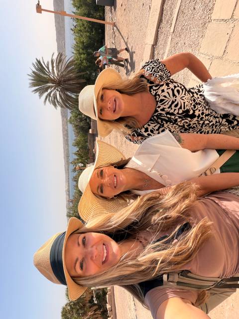 Three women in stylish hats posing with desert lake scenery behind