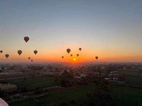 Sunrise panorama with numerous hot air balloons floating above Nile-side farmlands