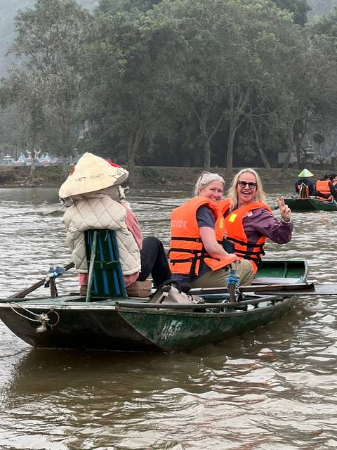 Tourists wearing life jackets smile on a small metal boat rowed along a calm river.