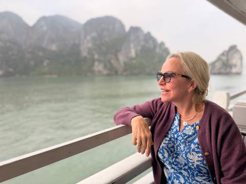 A woman relaxes on a cruise deck looking at the emerald waters and karst peaks of the bay.