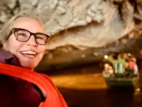 Smiling traveller in a dimly lit cave boat ride wearing a life vest.