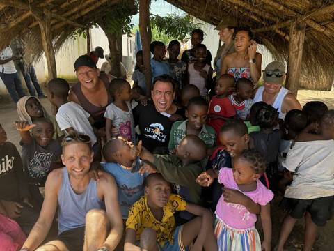 Tourists laughing and playing with local children under a thatched shelter.