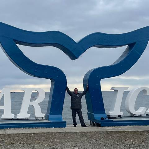 Traveler stretching arms beneath a giant blue whale-tail sculpture by the sea in Punta Arenas.