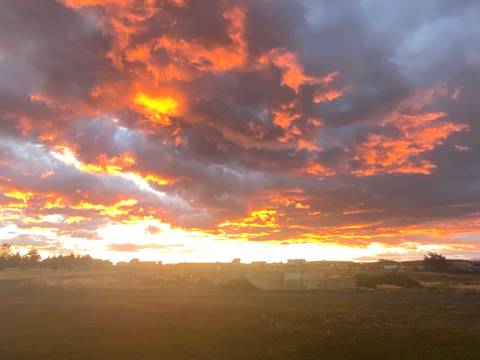 Fiery sunset clouds illuminate a flat Patagonian landscape with distant silhouettes of buildings.