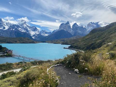 Turquoise lake framed by dramatic snow-capped peaks and a small lodge in Torres del Paine.