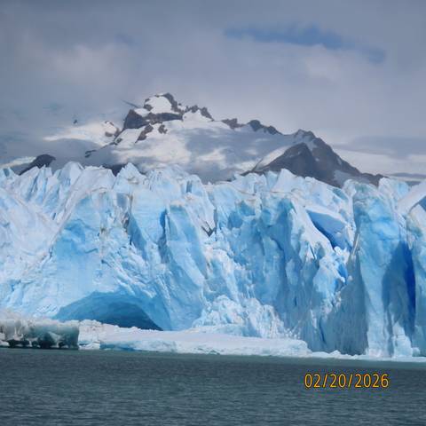 Massive blue glacier face with snowy mountains rising behind.