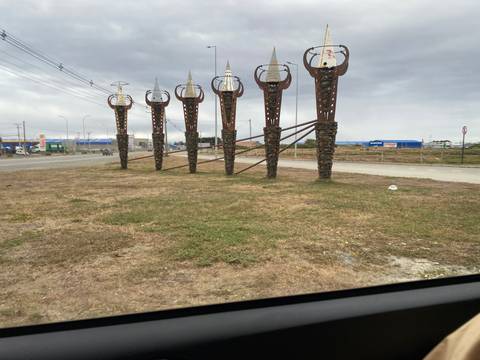 Roadside metal monument of spear-like sculptures on an overcast day, photographed from a vehicle.