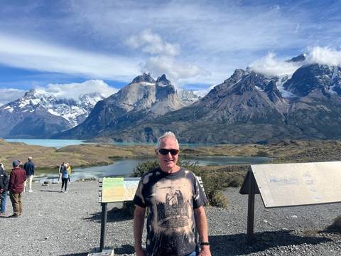 Traveller poses at a scenic viewpoint overlooking lakes and the jagged peaks of Torres del Paine while others admire the view.