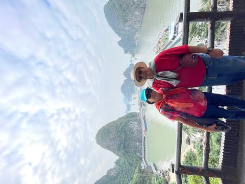 Couple posing on a viewpoint overlooking limestone karsts and green waters of Halong Bay under a cloudy sky.
