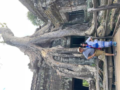 Couple posing beside massive strangler-fig roots engulfing an ancient stone doorway at a jungle ruin.