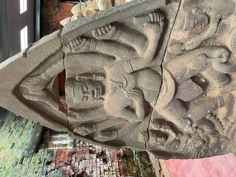 Ancient sandstone bas-relief of a multi-armed Hindu deity inside a brick temple structure