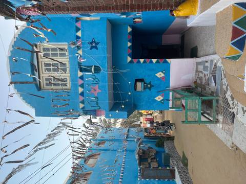 Bright blue Nubian house with mosaic walkway and festive streamers overhead.