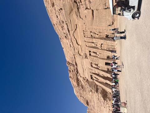Wide view of Abu Simbel's rock-cut facade with many visitors walking across the forecourt.