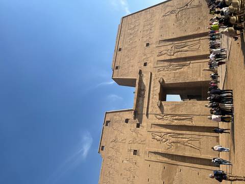 Grand pylon entrance of Edfu Temple adorned with reliefs, with groups of tourists below.