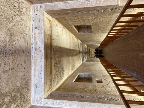 Long, decorated corridor inside an ancient Egyptian tomb with painted walls and ceiling.