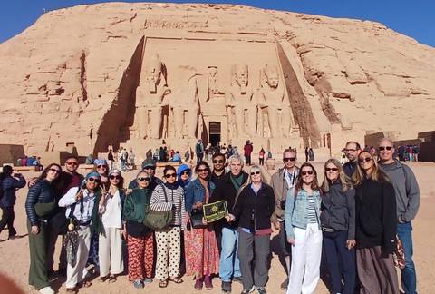 Large tour group posing in front of the monumental Abu Simbel rock-cut temple under bright desert sun.