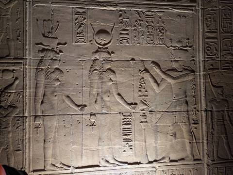 Detailed wall relief depicting ancient Egyptian figures with hieroglyphs, lit by spotlight.