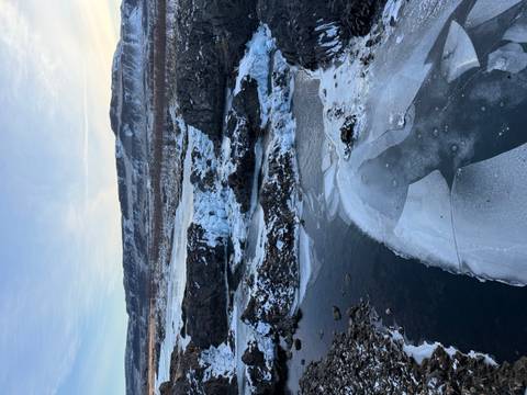 Partially frozen river and cascades winding through a rocky, snow-dusted valley under pale winter light.