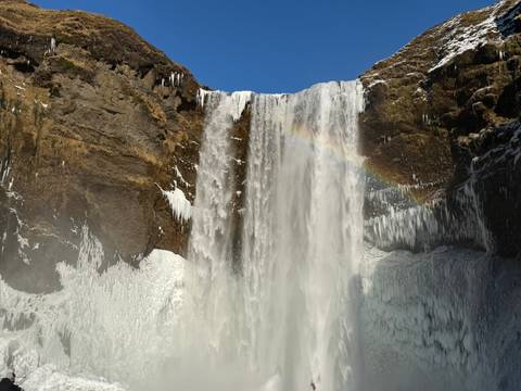 Powerful Skógafoss waterfall plunging over an icy cliff face with a rainbow arching through its mist.