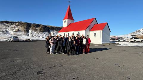 Large tour group posing in front of a white church with red roof on a snowy volcanic plain.
