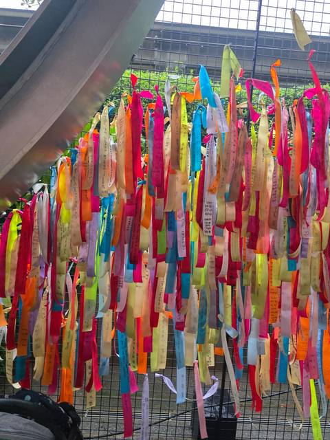 Dense curtain of brightly coloured ribbons with handwritten wishes hanging in rows.
