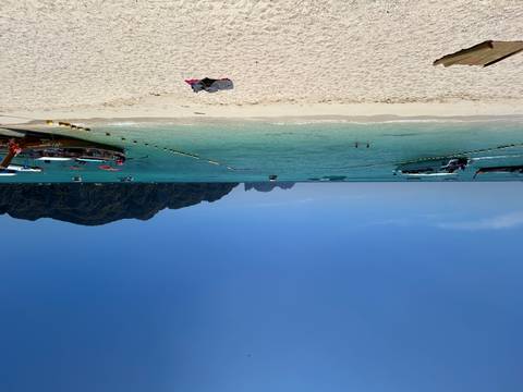 White-sand beach with long-tail boats and swimmers set before emerald sea and steep island cliffs.