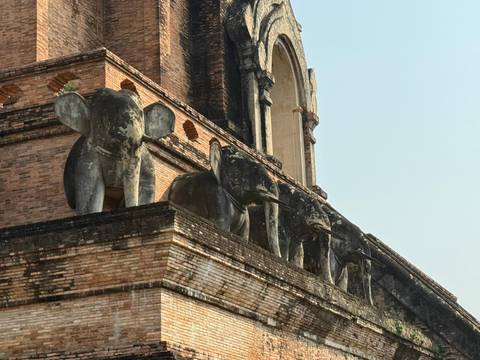 Ancient brick stupa decorated with stone elephant carvings jutting outward.