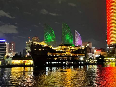 Illuminated sail-rigged dinner boat glides along the Saigon River against a vibrant city skyline at night.
