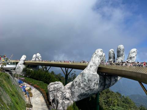 The iconic Golden Bridge held by giant stone hands stretches through misty mountains packed with visitors.
