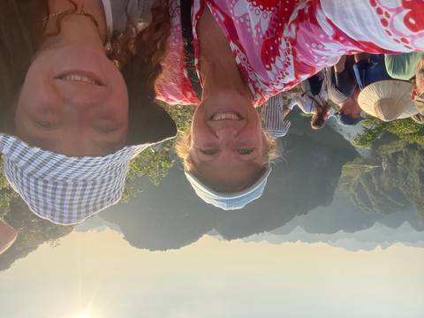 Travellers smile on a high lookout over layered limestone karsts bathed in warm late-day light.