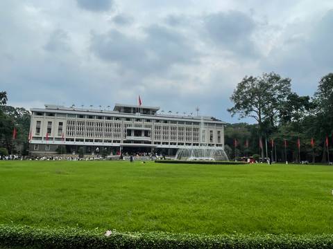 Wide lawn and fountain front the modernist Reunification Palace under partly cloudy skies.