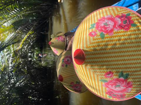 Bright floral conical hats seen from behind while gliding through narrow, palm-shaded waterways.