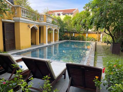 Charming yellow-walled boutique hotel courtyard with a tranquil swimming pool and sun-loungers surrounded by greenery.