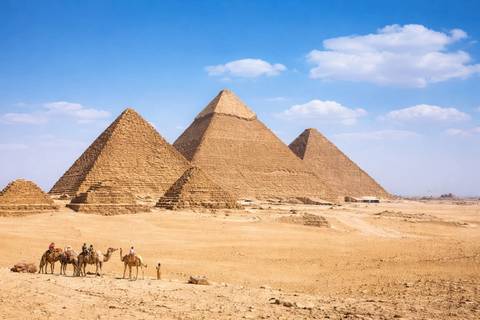 Panoramic view of the three pyramids of Giza with camel riders in the sandy foreground