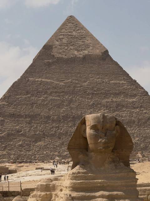 Sphinx head in foreground with the towering pyramid steps rising behind