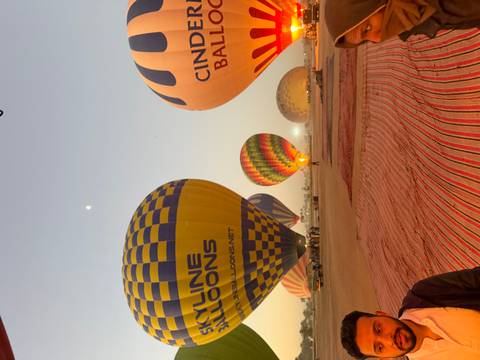 Row of brightly coloured hot-air balloons being inflated at dawn on a desert launch field.