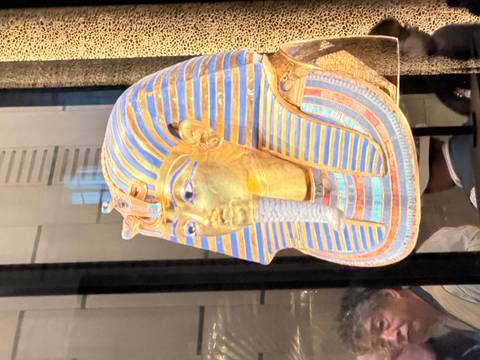 Golden mask of Tutankhamun displayed behind glass inside a museum gallery.