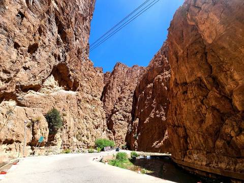 Dramatic red sandstone walls towering above narrow road through Todra Gorge under bright sky.