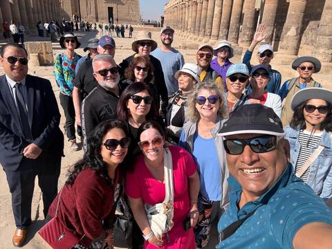 Wide selfie of a large tour group smiling in front of ancient stone columns at an Egyptian temple.