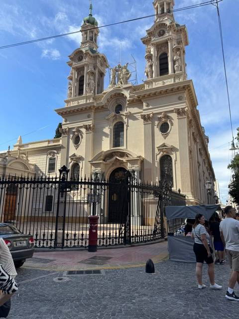 Historic sandstone church facade bordered by wrought-iron fencing on a sunny urban street