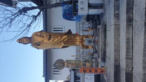 Tall golden Kannon statue at a Japanese temple surrounded by smaller figures and stone steps.