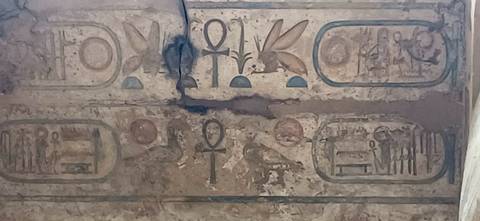 Weathered wall section with faded ankh and cartouches among damaged plaster