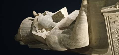 Side-lit colossal seated statue of a pharaoh at night against the dark sky