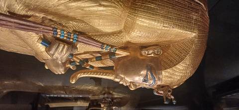 Golden sarcophagus of Tutankhamun with intricate inlay and blue accents displayed under museum lighting