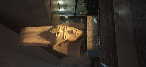 Illuminated colossal sandstone head of an ancient Egyptian pharaoh displayed in a modern museum hall