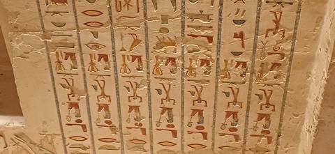 Close-up of painted hieroglyphic columns on a tomb wall with vivid reds and yellows.