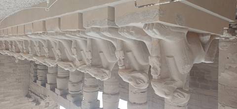 Row of ram-headed sphinxes lining the entrance corridor of an ancient sandstone temple.