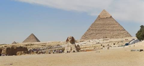 Panoramic desert scene with the Great Sphinx and two pyramids under a blue sky.