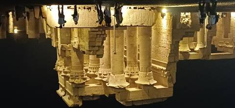 Ancient temple columns dramatically lit at night with visitor silhouettes in the foreground.