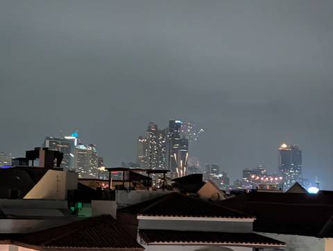 Nighttime city skyline with illuminated high-rise buildings beyond dark rooftops.